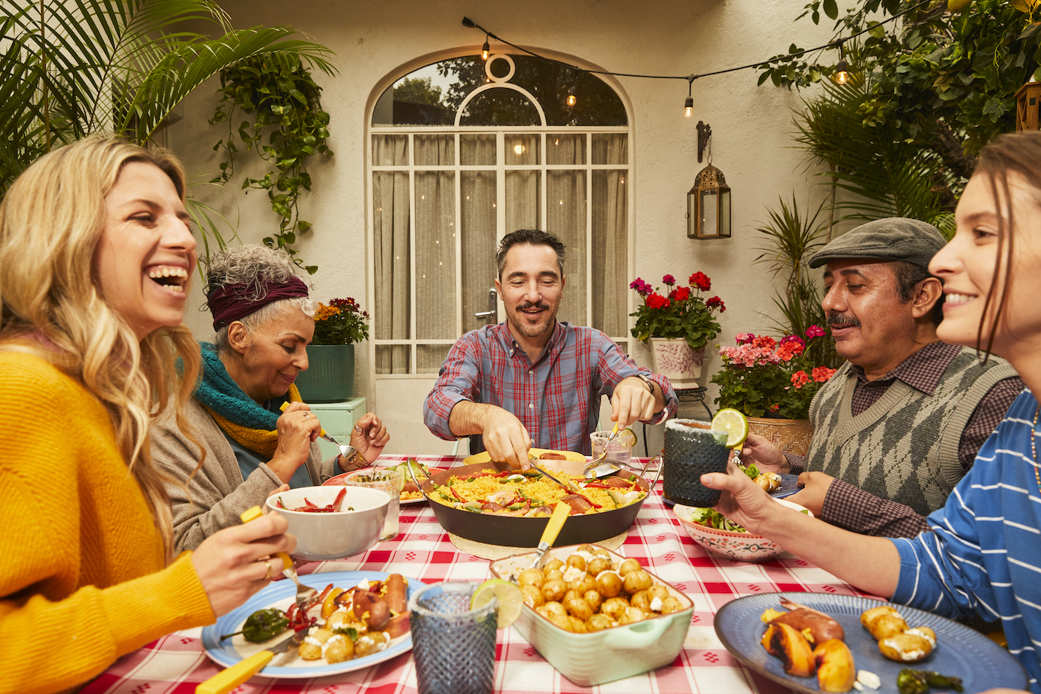 A group gathered outdoors sharing a meal with dishes like paella, potatoes, and vegetables.