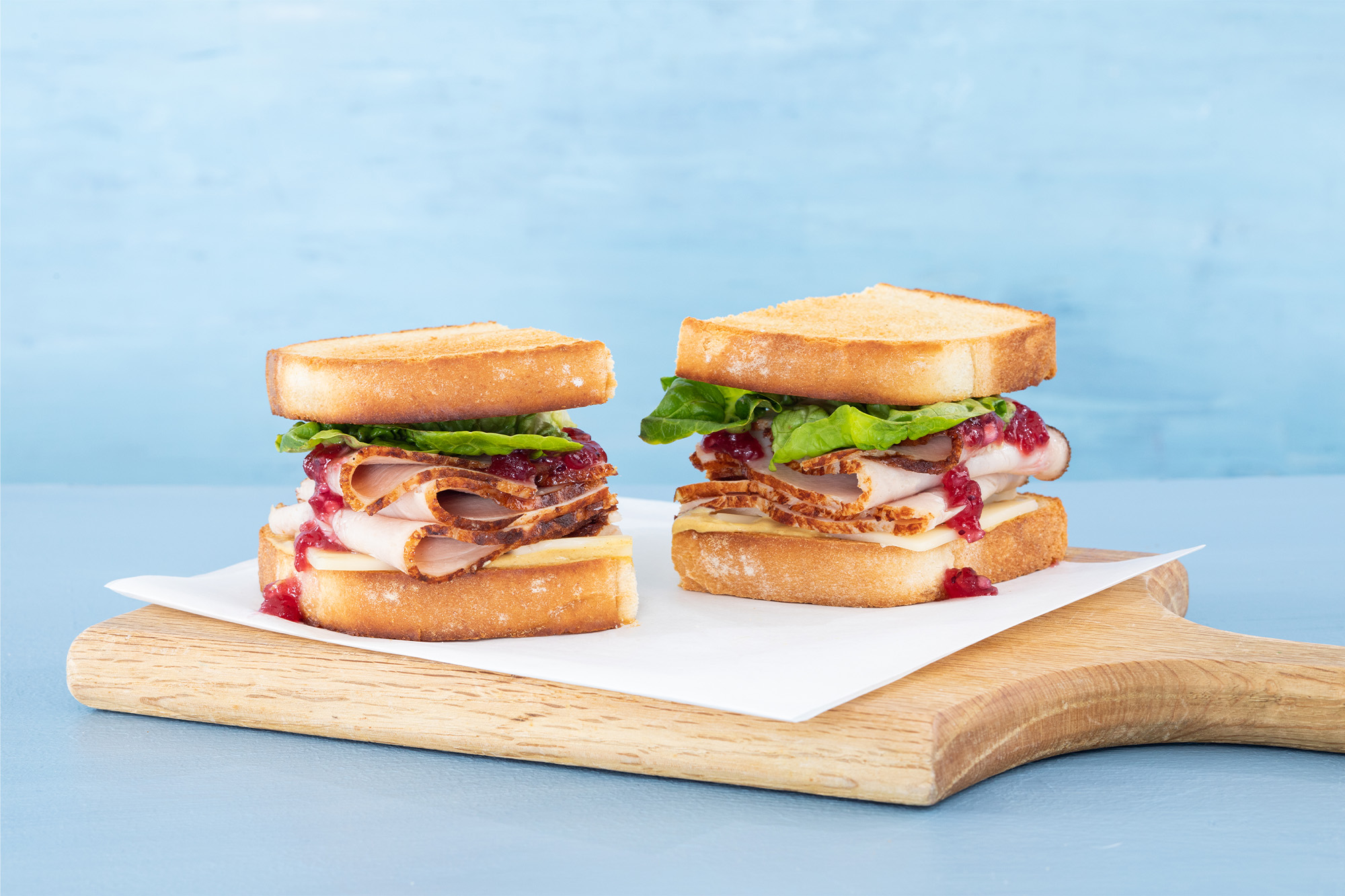 A turkey sandwich recipe with cranberry sauce, cheese, and lettuce on toasted bread, cut in half.