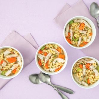 A comforting turkey soup recipe with egg noodles, carrots, and shredded turkey in white bowls.
