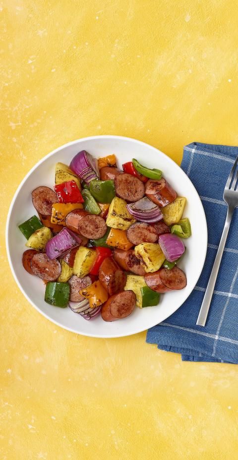 Bowl of turkey sausage, pineapple, peppers, and onions on yellow background with a blue napkin.