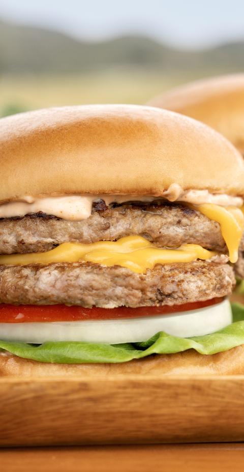 Three Butterball turkey cheeseburgers with lettuce, tomato, and onion served on a wooden tray.