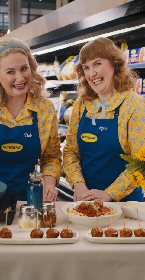 The Butterball Gals behind a free sample table with Butterball turkey meatballs on it, in the meat section of a grocery store. 