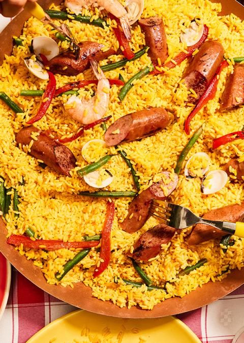 Paella with smoked turkey sausage, shrimp, clams, and veggies served on a red checkered tablecloth.