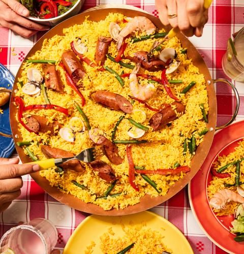 Paella with smoked turkey sausage, shrimp, clams, and veggies served on a red checkered tablecloth.