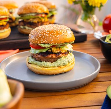 Agave-lime turkey burger with cheesy corn and avocado crema on a sesame bun, served on a plate.