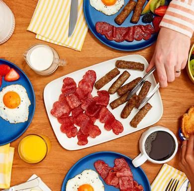 A person uses tongs to serve Butterball turkey bacon and turkey breakfast sausage on a dinner table.