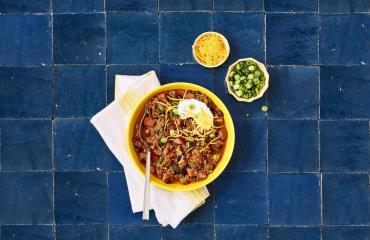 Chili in a bowl with two small side bowls on a blue tile table 