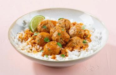 A bowl of Butterball coconut curry turkey meatballs served over rice with a slice of lime.