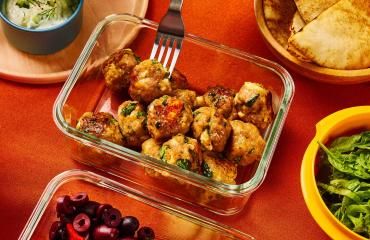 A person removes a Greek ground turkey meatball from a storage container with a fork.