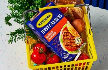 A six-patty pack of Butterball Original Seasoned Turkey Burgers in a basket of groceries.