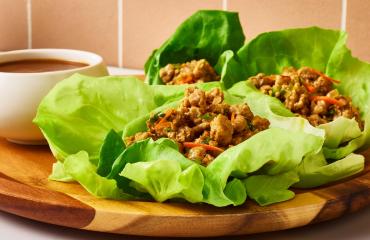 Butterball Thai ground turkey lettuce wraps on a plate next to a bowl of sauce.