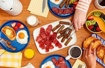 A person uses tongs to serve Butterball turkey bacon and turkey breakfast sausage on a dinner table.