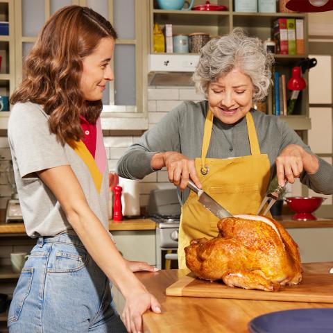 Passing down a family tradition as two generations prepare a roasted turkey for a shared meal.