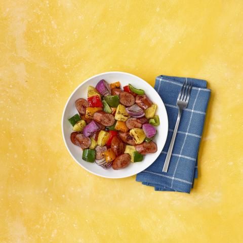 Bowl of turkey sausage, pineapple, peppers, and onions on yellow background with a blue napkin.