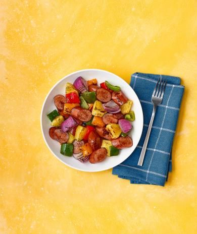 Bowl of turkey sausage, pineapple, peppers, and onions on yellow background with a blue napkin.