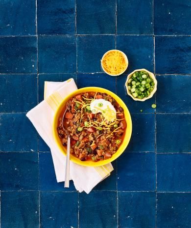 Turkey chili recipe in a yellow bowl, topped with sour cream, cheese, and green onions.