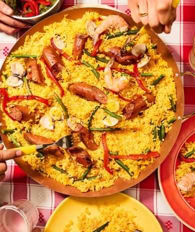 Paella with smoked turkey sausage, shrimp, clams, and veggies served on a red checkered tablecloth.