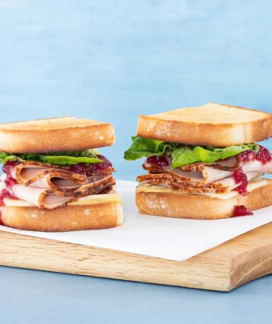 A turkey sandwich recipe with cranberry sauce, cheese, and lettuce on toasted bread, cut in half.