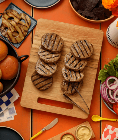 Grilled Butterball turkey patties on a wooden board with buns, fresh veggies, and burger toppings.