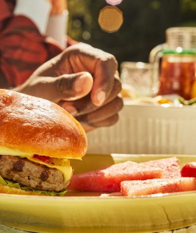 A burger and watermelon on a plate with picnic condiments in the background.