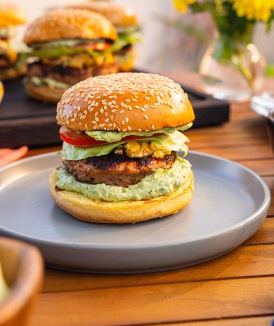 Agave-lime turkey burger with cheesy corn and avocado crema on a sesame bun, served on a plate.