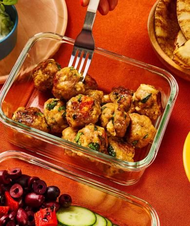 A person removes a Greek ground turkey meatball from a storage container with a fork.