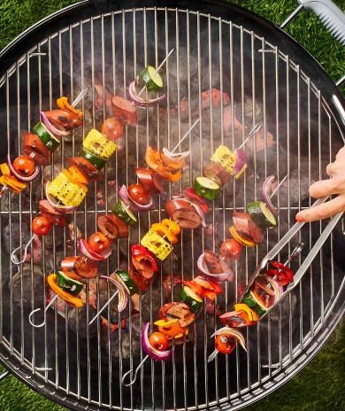 A person using tongs flips Butterball smoked sausage turkey kebabs on a grill.