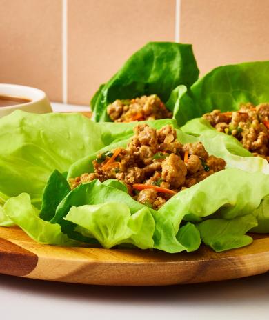 Butterball Thai ground turkey lettuce wraps on a plate next to a bowl of sauce.