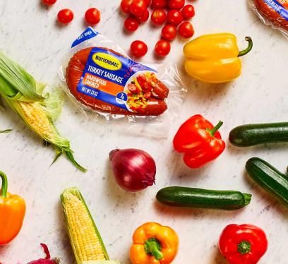 Two packs of Butterball Hardwood Smoked Turkey sausage on a counter next to a variety of vegetables.