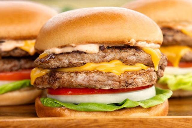 Stacked turkey cheeseburgers with lettuce, tomato, onion, and melted cheese on a soft bun.