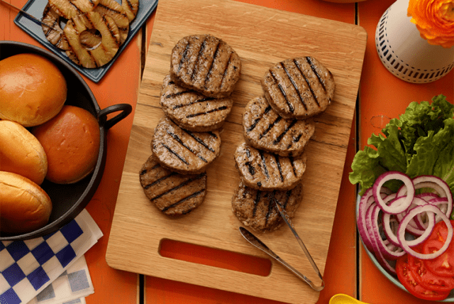 Grilled Butterball turkey patties on a wooden board with buns, fresh veggies, and burger toppings.