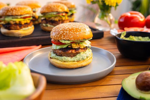 Agave-lime turkey burger with cheesy corn and avocado crema on a sesame bun, served on a plate.