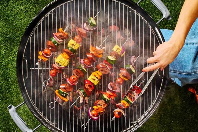 A person using tongs flips Butterball smoked sausage turkey kebabs on a grill.